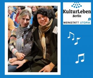 Eine rechteckige Bildtafel in blauer Farbe: Links sieht man das weißgerahmte Foto von Angela Meyenburg, Geschäftsführerin von KulturLeben Berlin und KulturLeben-Mitarbeiterin Liudmyla sitzend in einem Innenraum. Angela hat schwarze gelockte Haare. Sie trägt und einen schwarzen Wintermantel und einen hellbraunen Schal. Links neben ihr im Bild sitzt Liudmyla mit blondem Haar, einem blau-weiß-rosa gestreiften Pullover und einem grauen Schal. Beide Frauen lachen in die Kamera. Hinter ihnen sitzen Menschen in mehreren Reihen. Wir befinden uns in einem Konzertsaal. Rechts vom Foto sieht man in der oberen rechten Ecke das Logo der Werkstatt Utopia. Darunter befinden sich drei weiße stilisierte Achtelnoten vor dem blauen Hintergrund der Bildtafel.